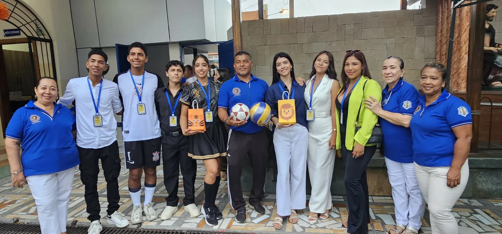 Estudiantes, docentes y personal con balones y reconocimientos deportivos en el ingreso de la institución