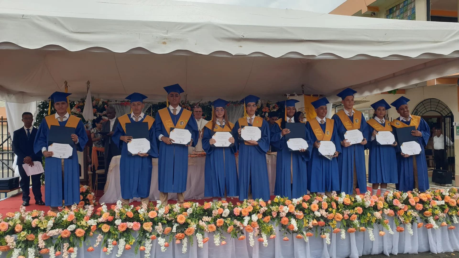 Bachilleres con toga y birrete azul muestran sus títulos en la ceremonia de grado