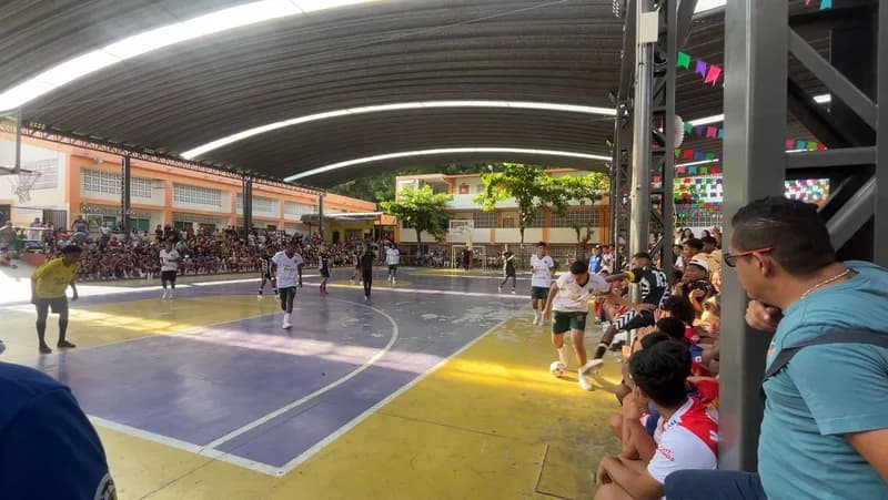 Partido de fútbol sala en la cancha cubierta de la institución, con estudiantes en las gradas